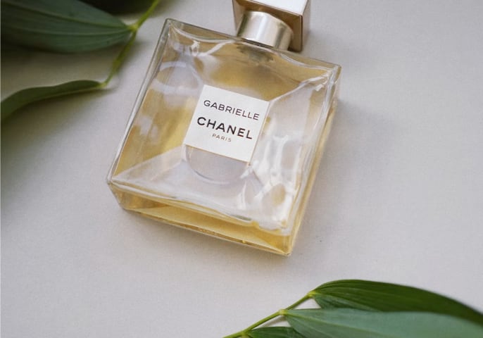 Golden perfume bottle laying flat on a table between green foliage